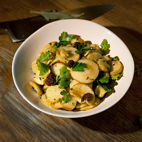 Dish of sliced parsnips sprinkled with goldenberries and topped with parsley and celery leaf