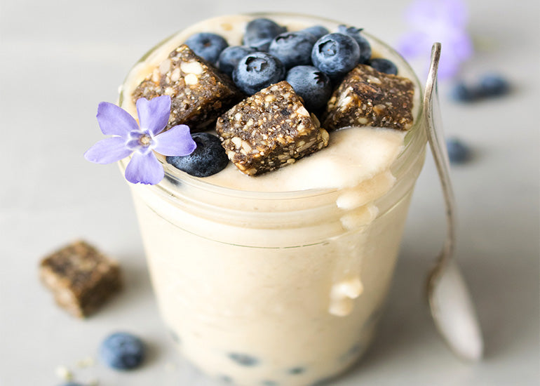 A creamy smoothie made with Navitas Organics Maca Powder in a glass mason jar, topped with Navitas Organics Blueberry Hemp Power Snacks and fresh blueberries.