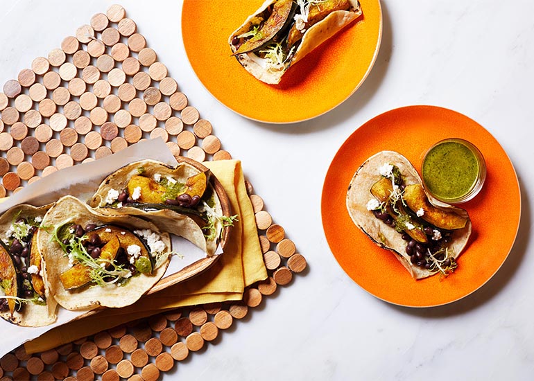 Plates topped with pumpkin black bean tacos with a cilantro lime sauce made with Navitas Organics Superfood+ Greens Blend.