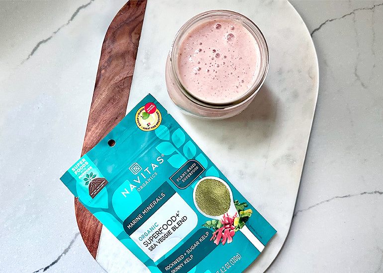 A smoothie made with Navitas Organics Superfood+ Sea Veggie Blend in a glass on a marble cutting board.