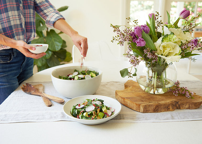 A woman sprinkling Navitas Organics Goji Berries on top of a bowl of green salad.