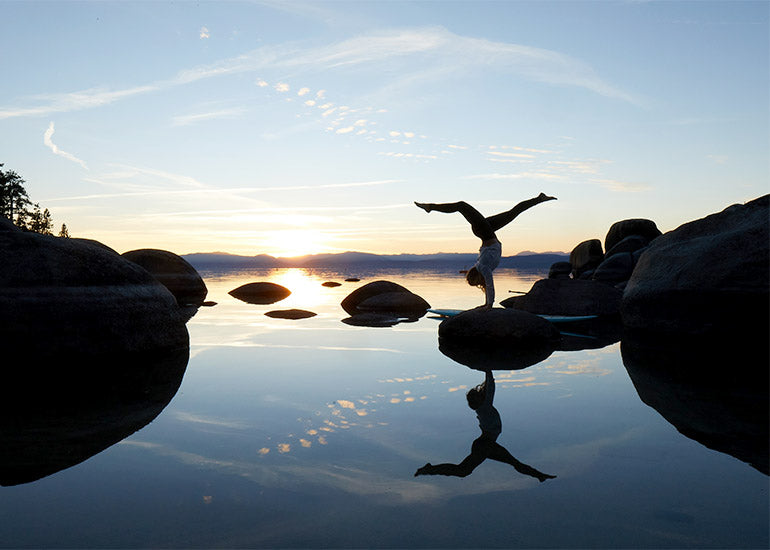 Woman doing a handstand on a rock over the ocean against the sunset