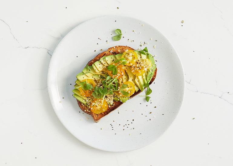 Avocado toast on a plate, topped with herbs, tomatoes and Navitas Organics Hemp Seeds.