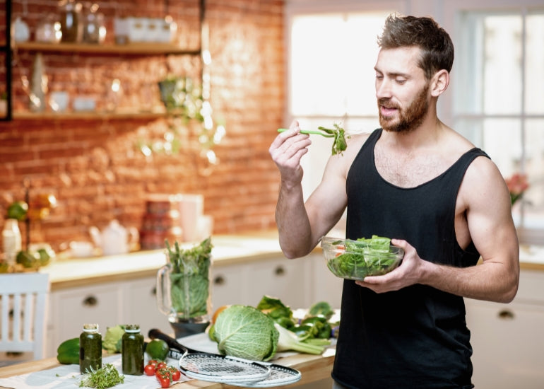 A young, athletic man eating greens out of a bowl in his kitchen