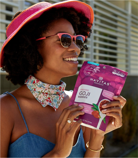 A woman in sunglasses and hat holding a bag of Navitas Organics Goji berries