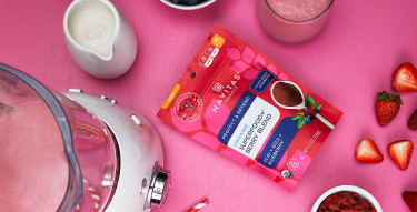 Package of Superfood Berry Blend on a counter with a blender and fresh fruit.